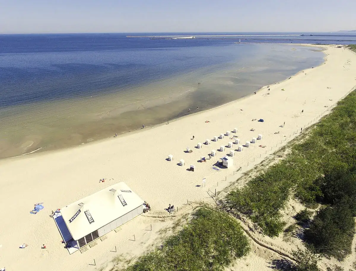 Szeroka, piaszczysta plaża z rzędami koszy plażowych i namiotem. W oddali widać morze i falochron. To najszersza plaża w Polsce.