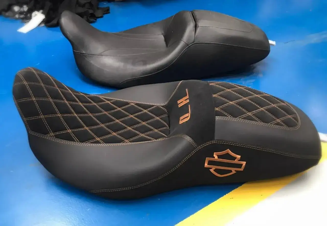 Due selle personalizzate moto in pelle nera con cuciture a rombi color rame e logo Harley-Davidson.