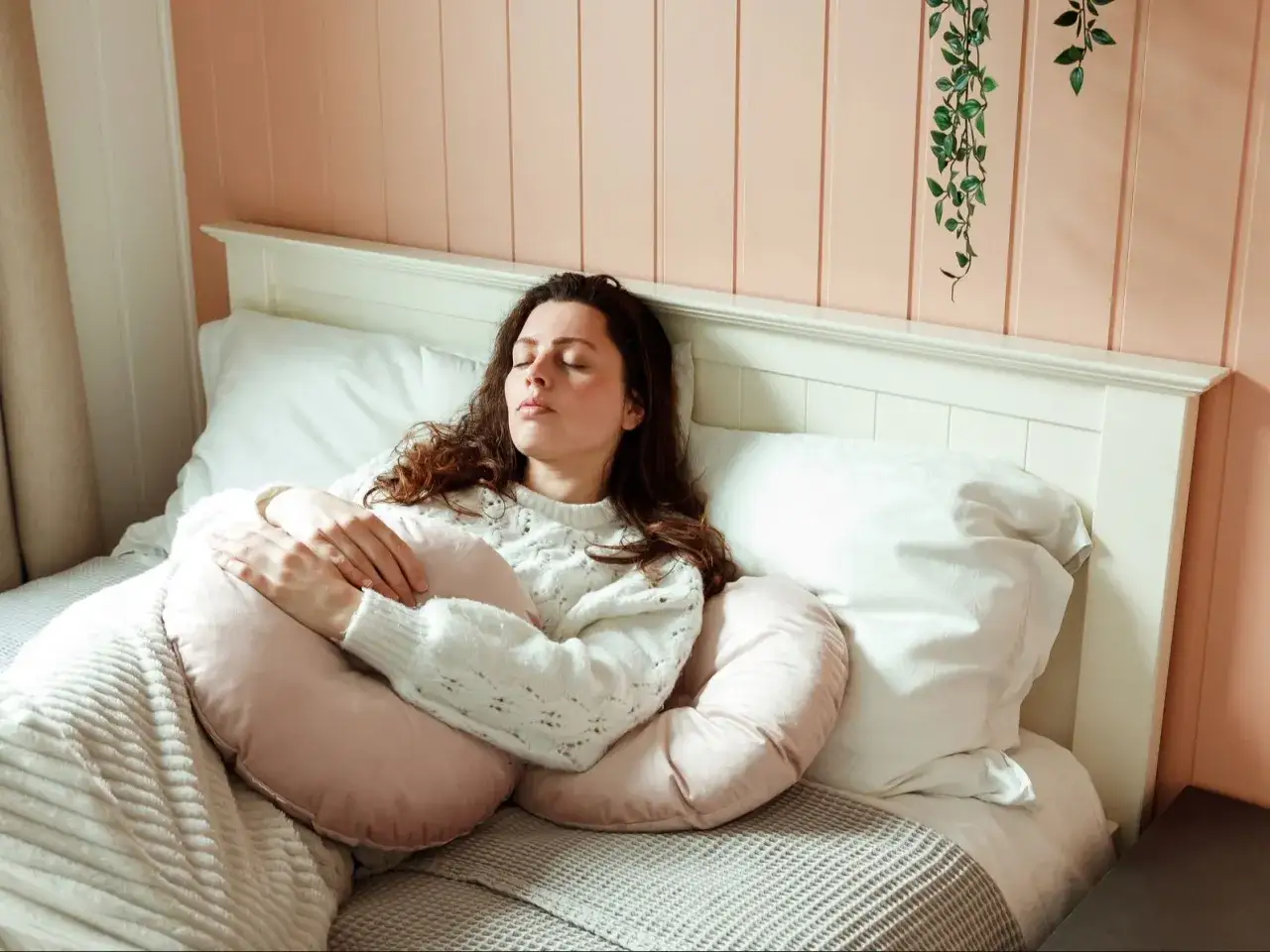 A woman is sleeping peacefully in bed, embracing a pink pillow. She's surrounded by white pillows, creating a cozy nest for sleeping with 3 pillows.