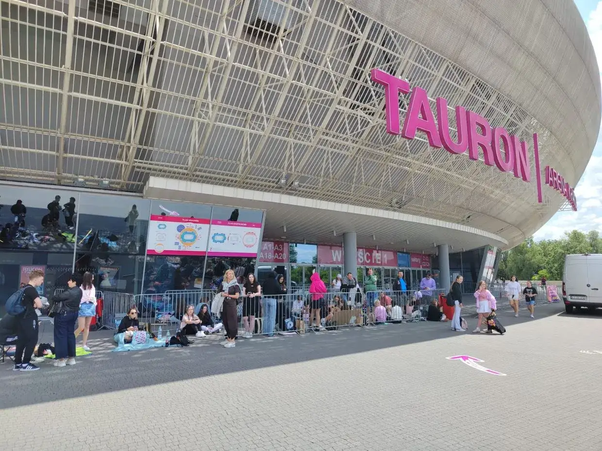 Fani czekają na festiwal ekipy 2026 przed Tauron Areną. Tłum ludzi siedzi i stoi w kolejce.