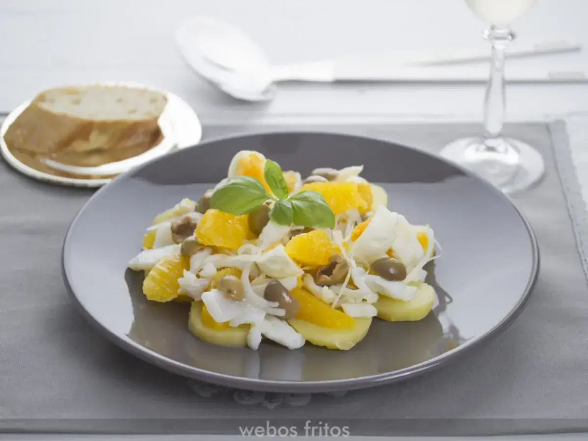 Ensalada malague&ntilde;a con patatas, naranja, huevo duro, aceitunas y bacalao desmigado, decorada con albahaca.