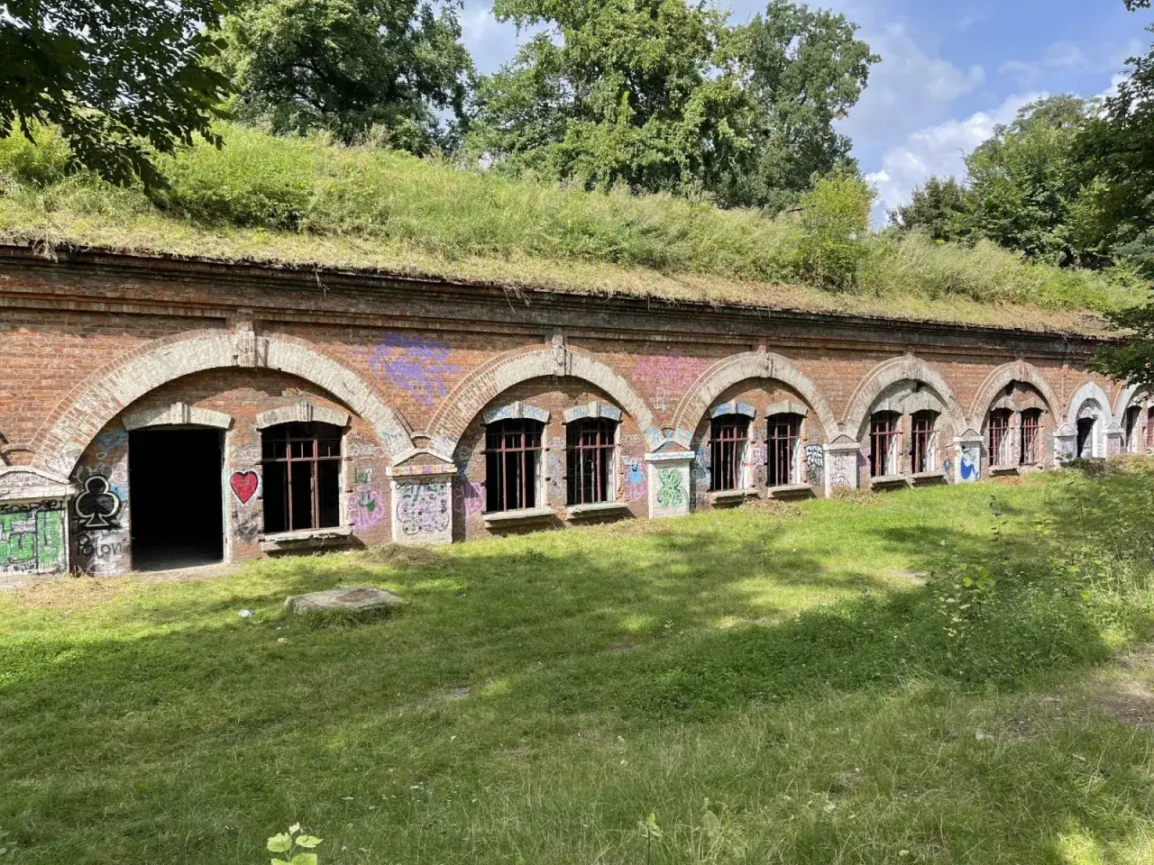 Zabytkowy Fort Bema, ceglana budowla z łukowymi oknami, porośnięta trawą i ozdobiona graffiti.