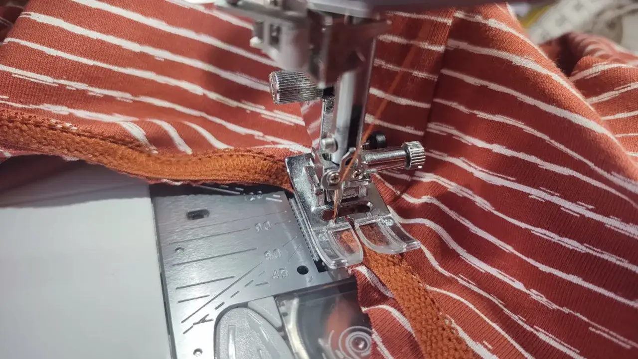 Machine à coudre en train de coudre un élastique sur un tissu rayé orange et blanc.