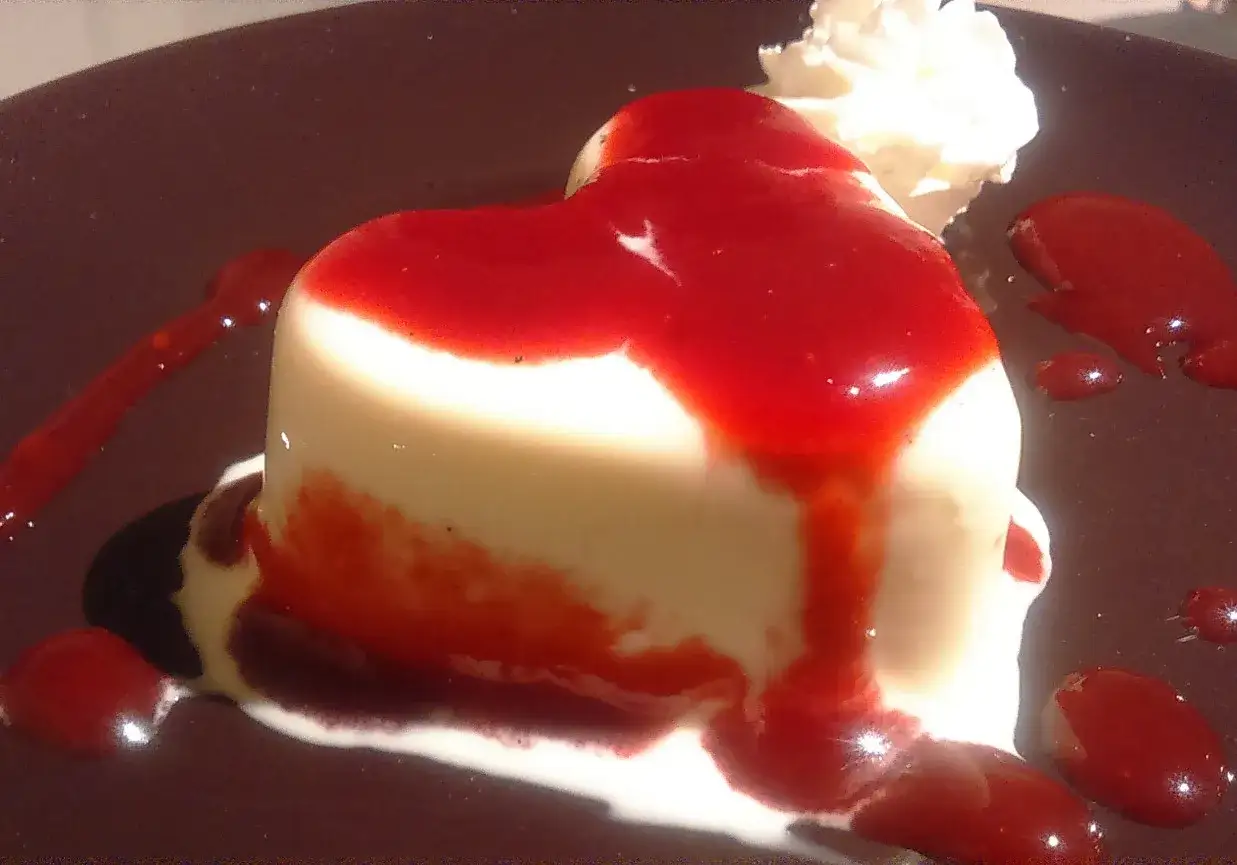 Serce z panna cotta polane sosem truskawkowym, ozdobione bitą śmietaną.