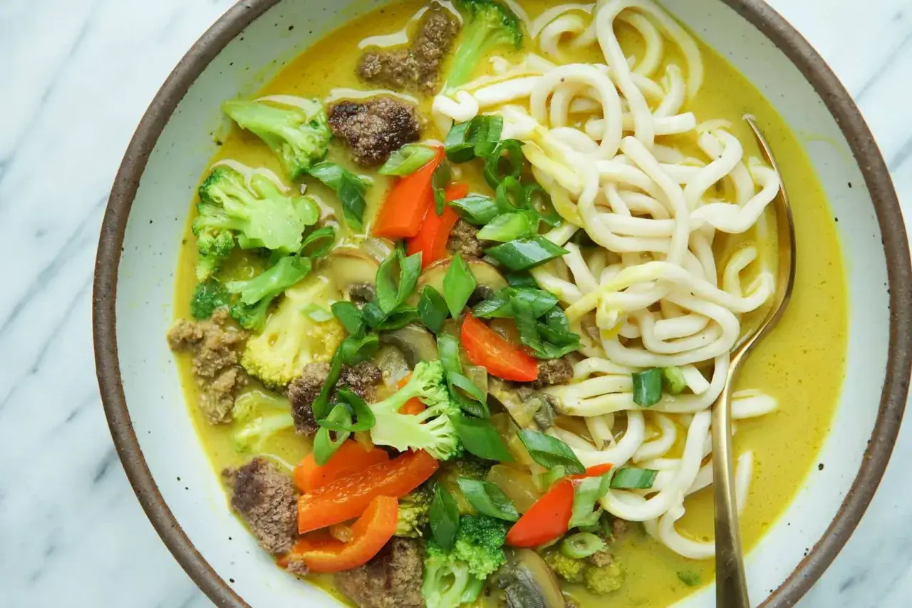 Aksamitny makaron z mlekiem kokosowym i curry, z kawałkami mięsa, brokułów, papryki i grzybów.