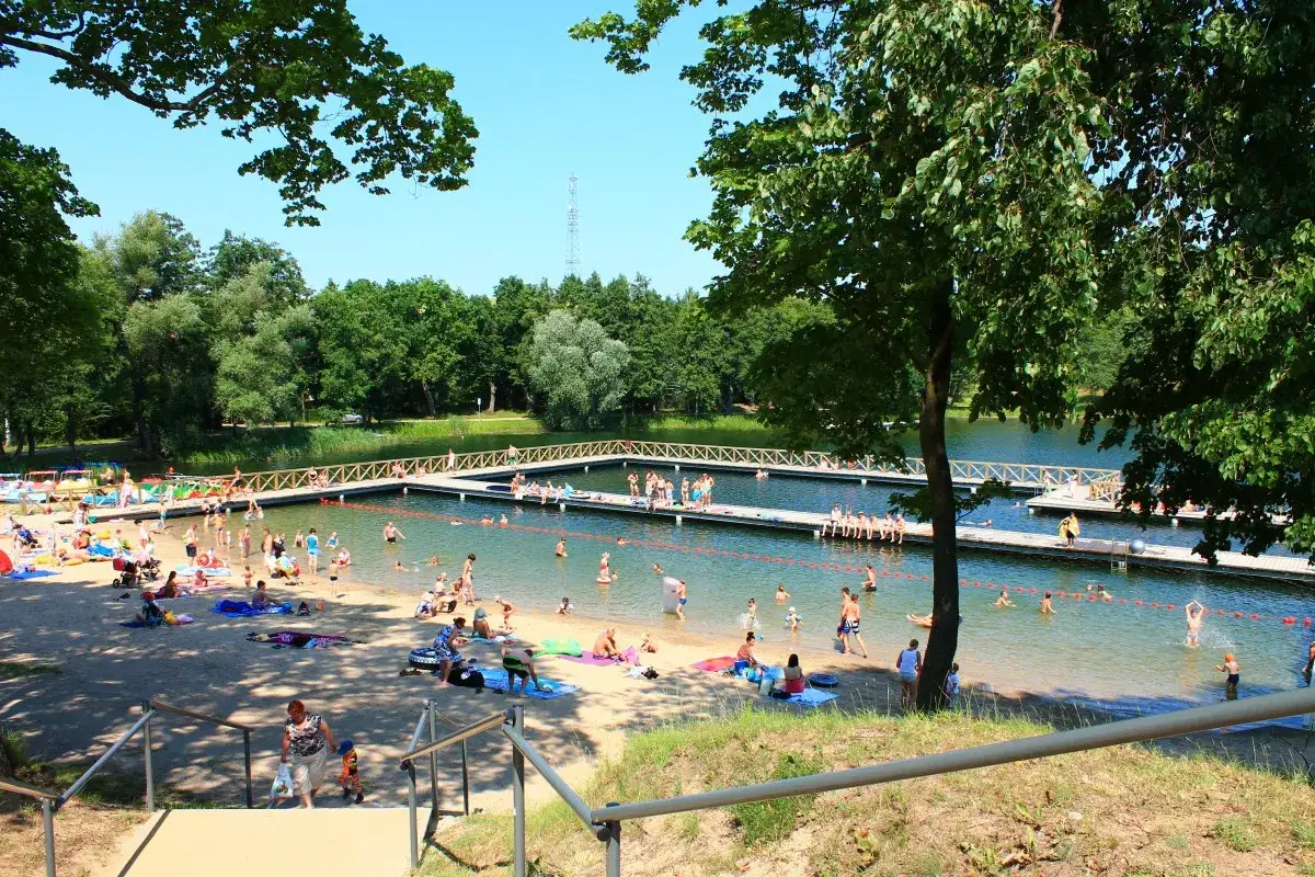Słoneczny dzień nad jeziorem, gdzie mnóstwo ludzi korzysta z kąpieli i plażowania. To idealne miejsce na letnie atrakcje dla dzieci.