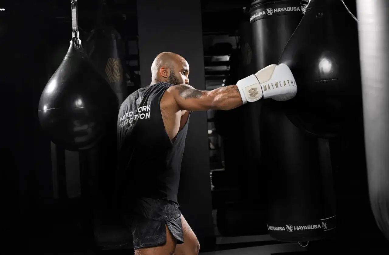 Floyd Mayweather training, throwing a punch at a heavy bag in a dark gym. His white glove bears his name.