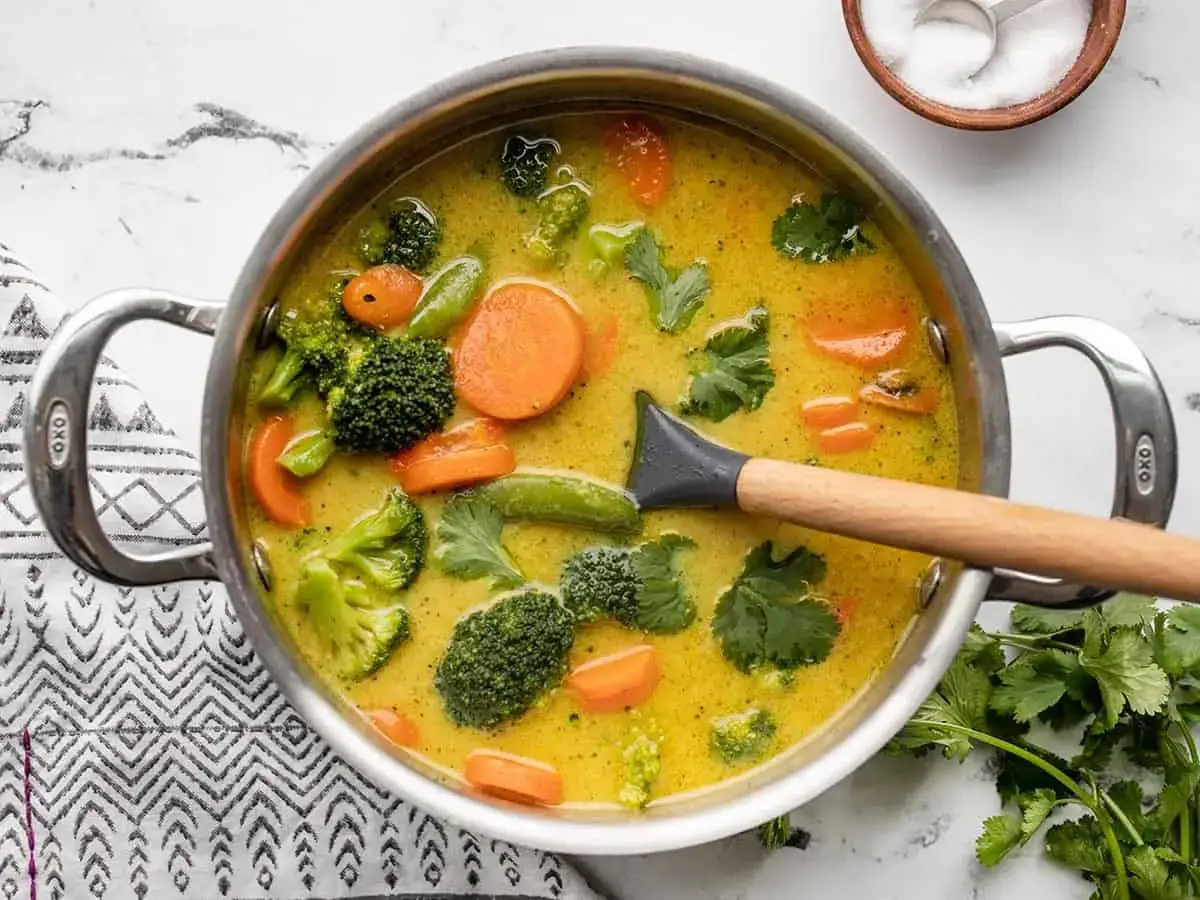 Un plat de curry v&eacute;g&eacute;tarien mijote dans une casserole, avec du brocoli, des carottes et des pois mange-tout.
