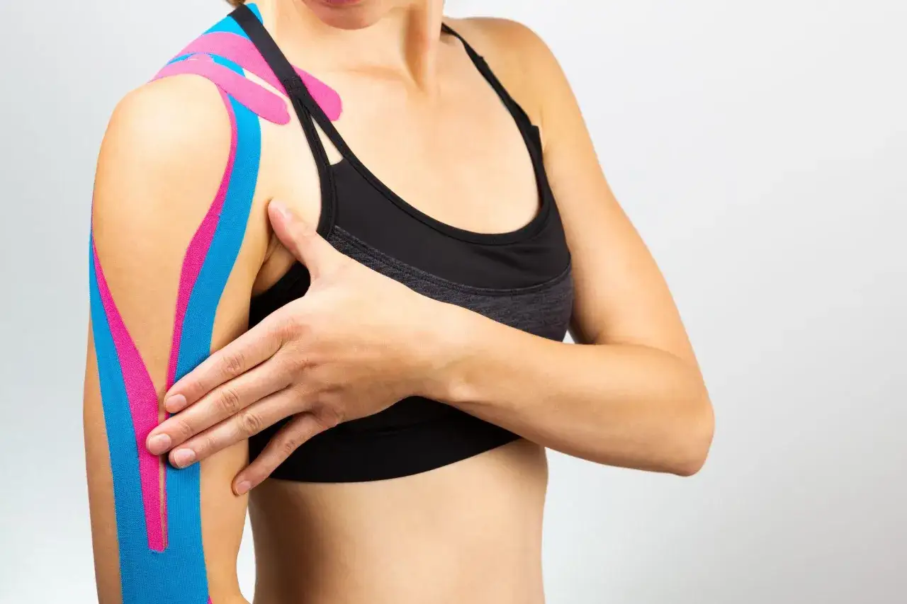 Mujer con bandas kinesiologicas rosas y azules en el hombro y brazo, mostrando c&oacute;mo se aplican para soporte deportivo.