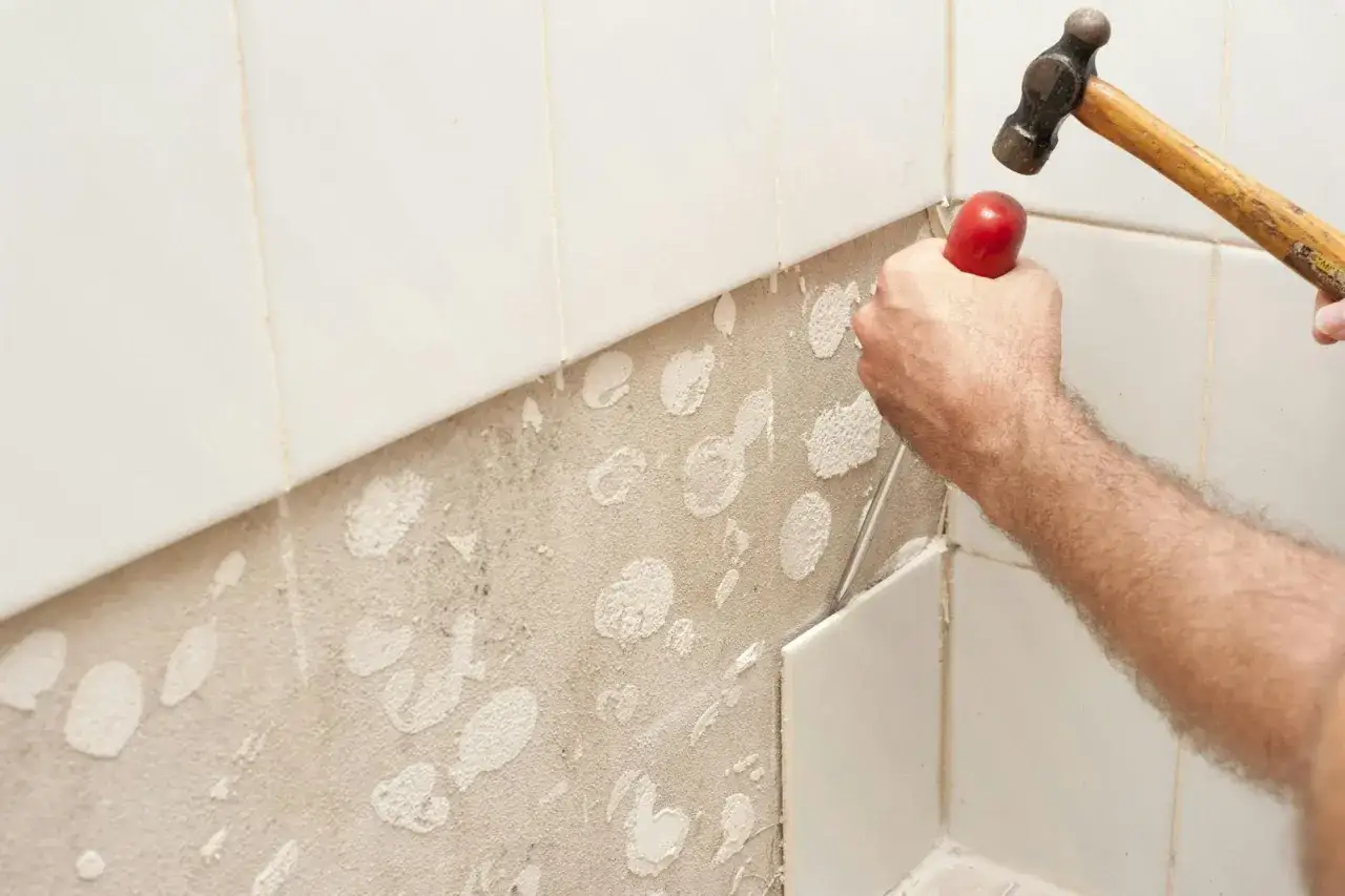 Mano golpeando cincel para quitar azulejos viejos de la pared.