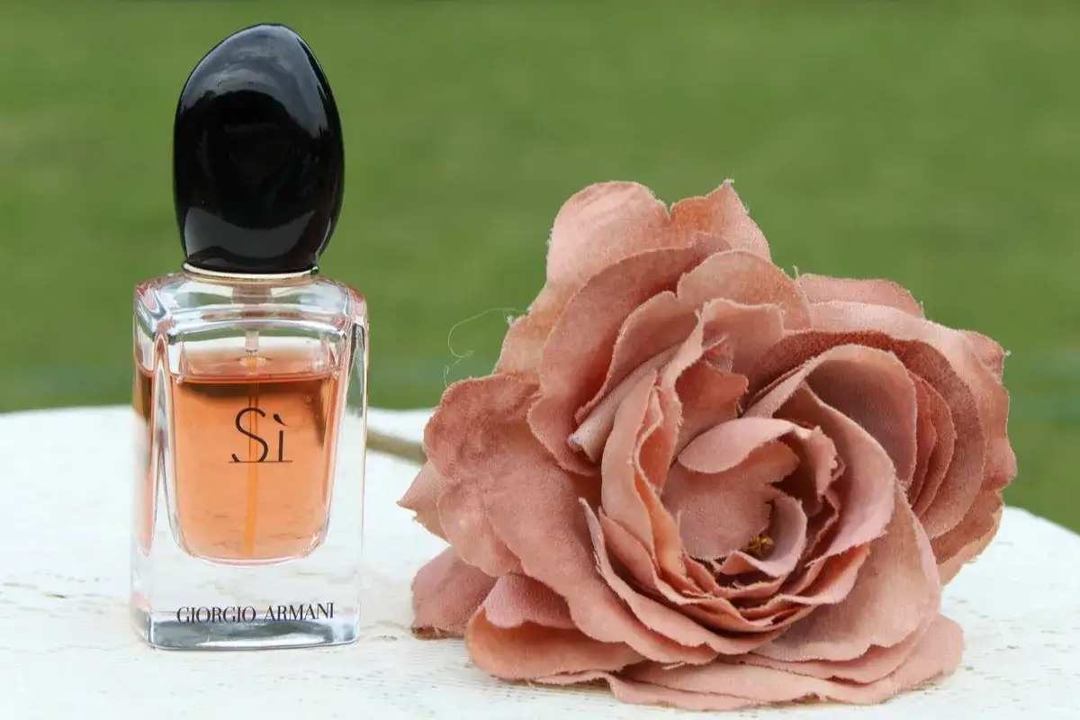 Elegancki flakon Giorgio Armani Si 100ml obok pudrowej róży.