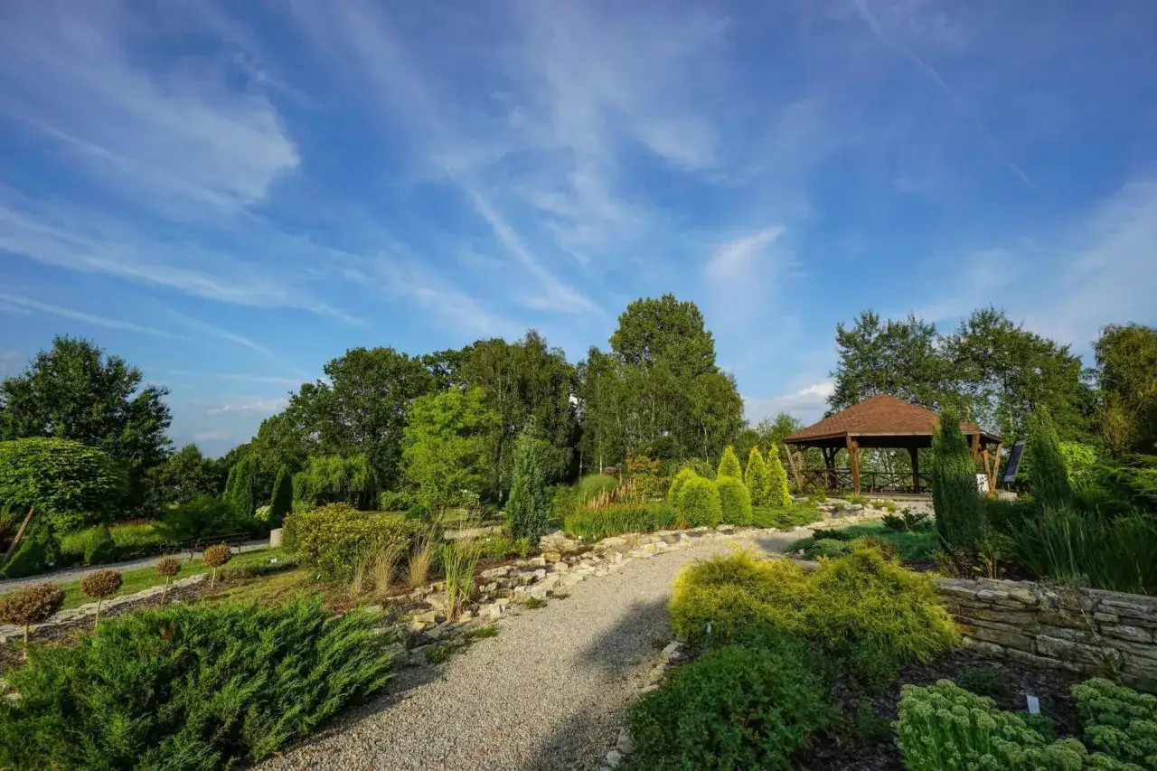 Piękne ogrody botaniczne na Śląsku z altaną i kamiennymi ścieżkami, otoczone bujną zielenią i błękitnym niebem.