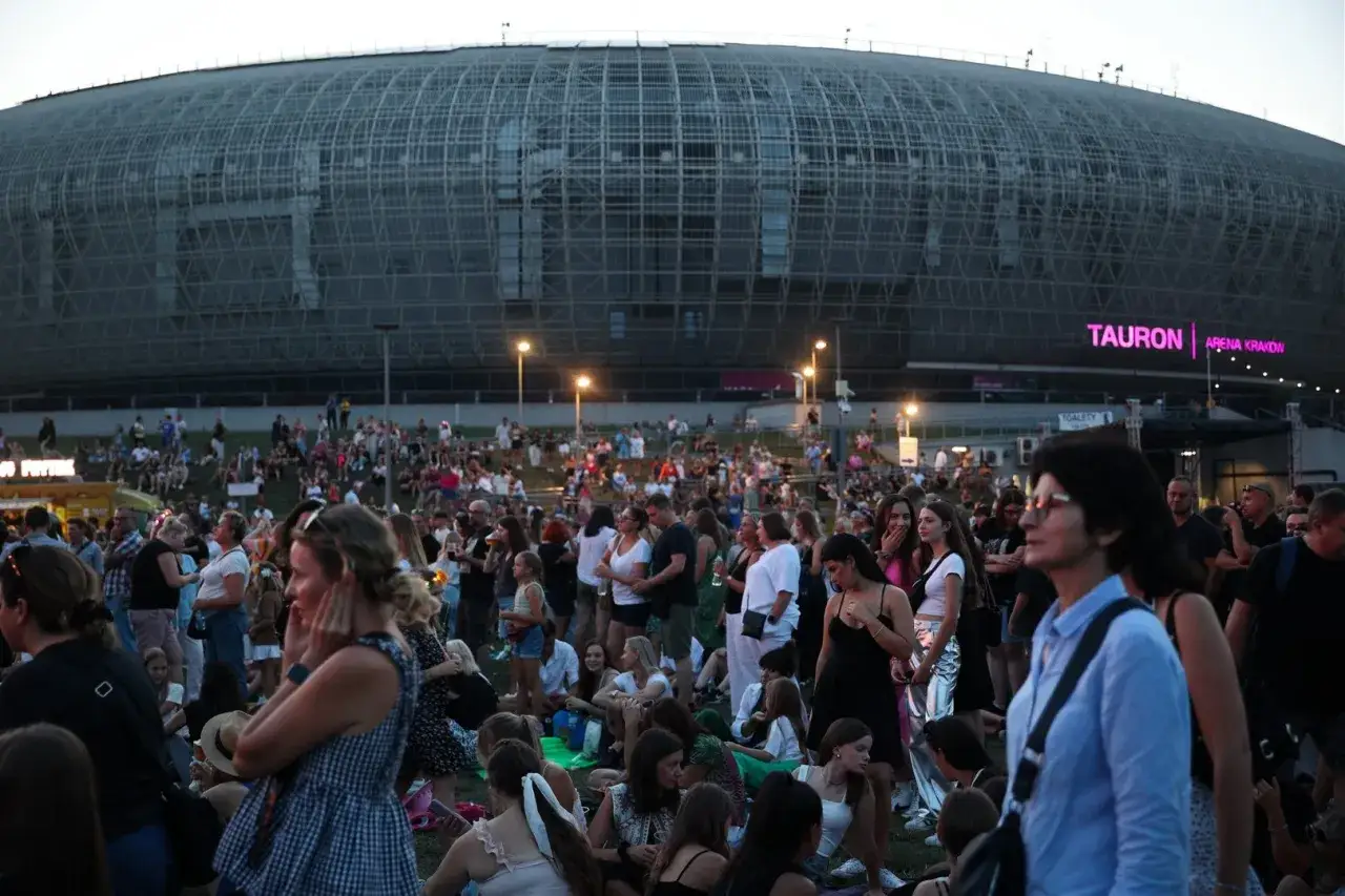 Tłum ludzi czeka na Tauron Arena koncerty. Widok na nowoczesną architekturę obiektu i rozświetlony napis.