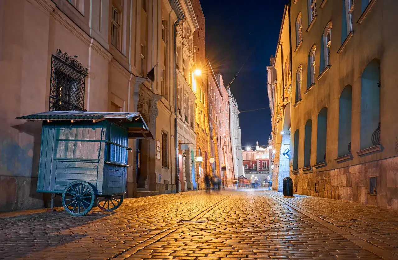 Nocna uliczka w Krakowie, oświetlona latarniami, z brukiem i starymi kamienicami. Czy jest krakow safe? Tak, wieczorem też.