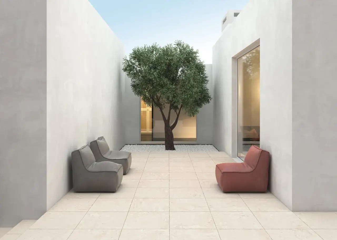 Patio moderno con suelo de **porcel&aacute;nico que es** de tonos claros, un &aacute;rbol frondoso en el centro y sillones de dise&ntilde;o.