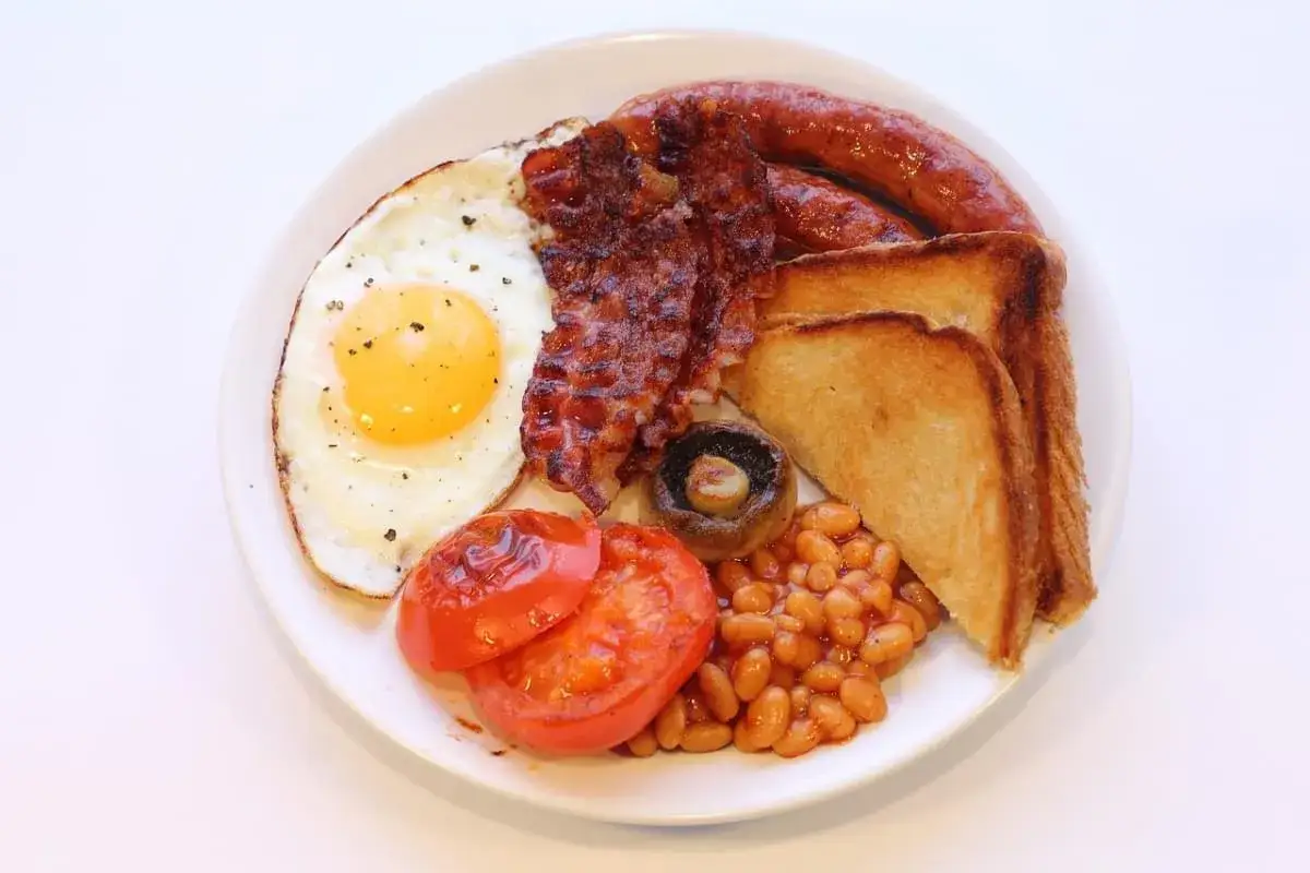 Un piatto tipico inglese con uovo fritto, bacon croccante, salsiccia, fagioli stufati, pomodori grigliati, fungo e toast.