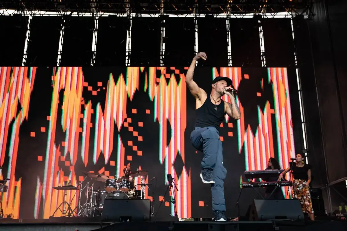 Residente en pleno concierto en España, con un fondo de luces vibrantes y un baterista en acción.