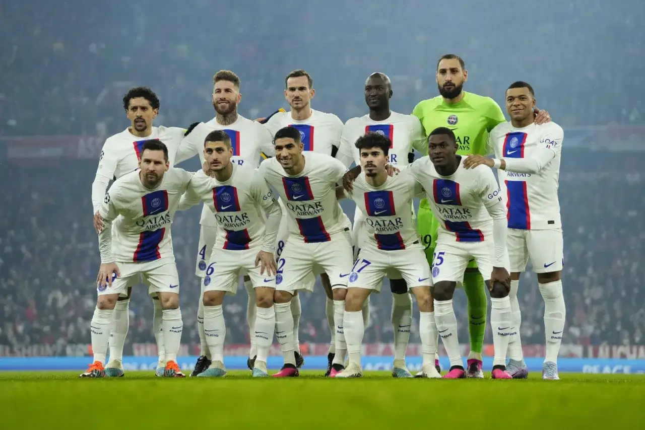 Aktualny skład PSG: Messi, Mbappé, Ramos i reszta drużyny w białych strojach na zielonej murawie.