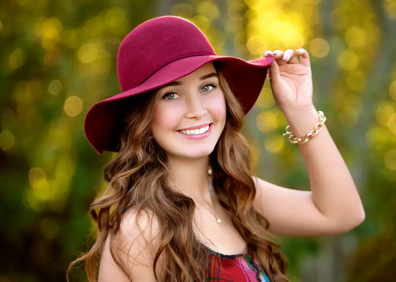 Ragazza sorridente con cappello bordeaux, capelli castani mossi, gioielli dorati. Perfetta per chi cerca azioni Photoshop gratis per ritocchi naturali.