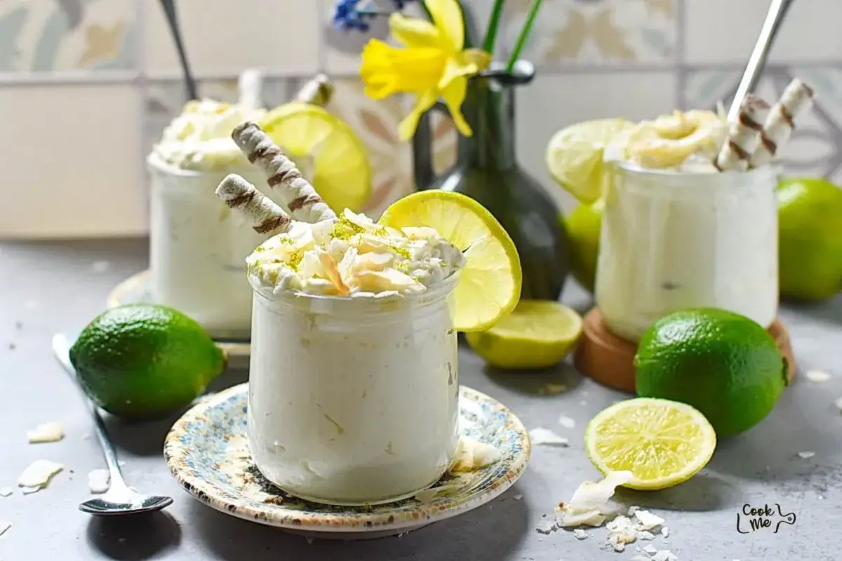 Delicioso mousse de coco y lima en vasitos, decorado con coco rallado, rodajas de lima y barquillos.