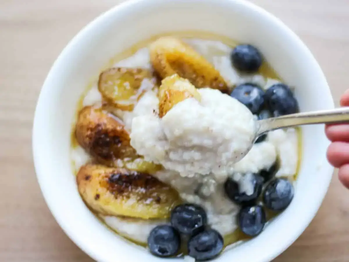Cremiges Buchweizen Porridge mit karamellisierten Bananen und Blaubeeren, serviert in einer weißen Schüssel. Ein Löffel voller Genuss.