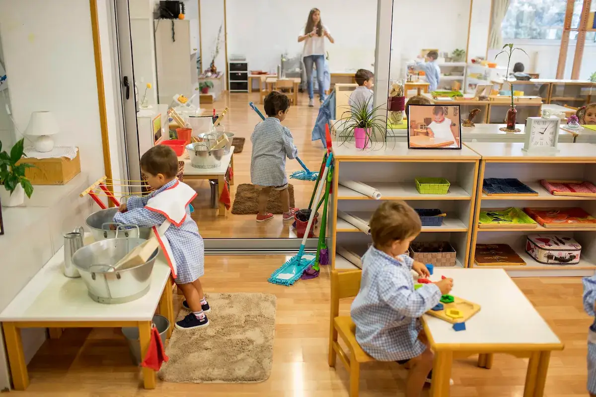 Ni&ntilde;os aprendiendo en un colegio Montessori: uno lava, otro barre, y otro juega con bloques.