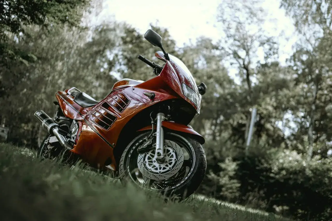 Czerwony motocykl Suzuki RF 900 na trawie, w tle drzewa. Poznaj suzuki rf 900 dane techniczne.
