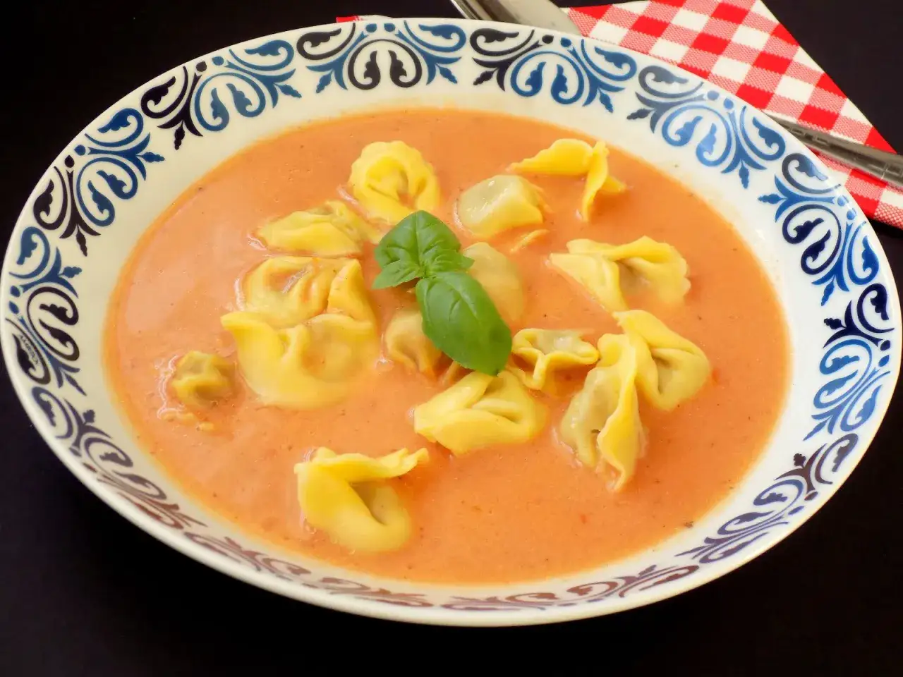 Zupa solferino z tortellini i listkiem bazylii w ozdobnej misce.