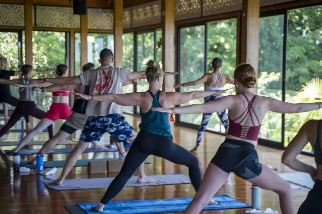 En grupp m&auml;nniskor ut&ouml;var yoga p&aring; svenska i en ljus lokal med stora f&ouml;nster.