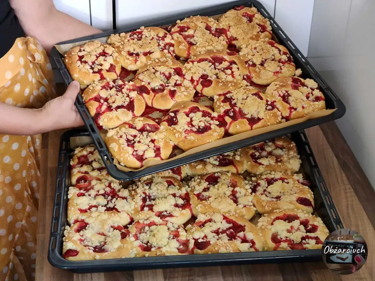 Dwie blachy pełne pysznych, domowych drożdżówek z truskawkami i kruszonką, gotowe do pieczenia.