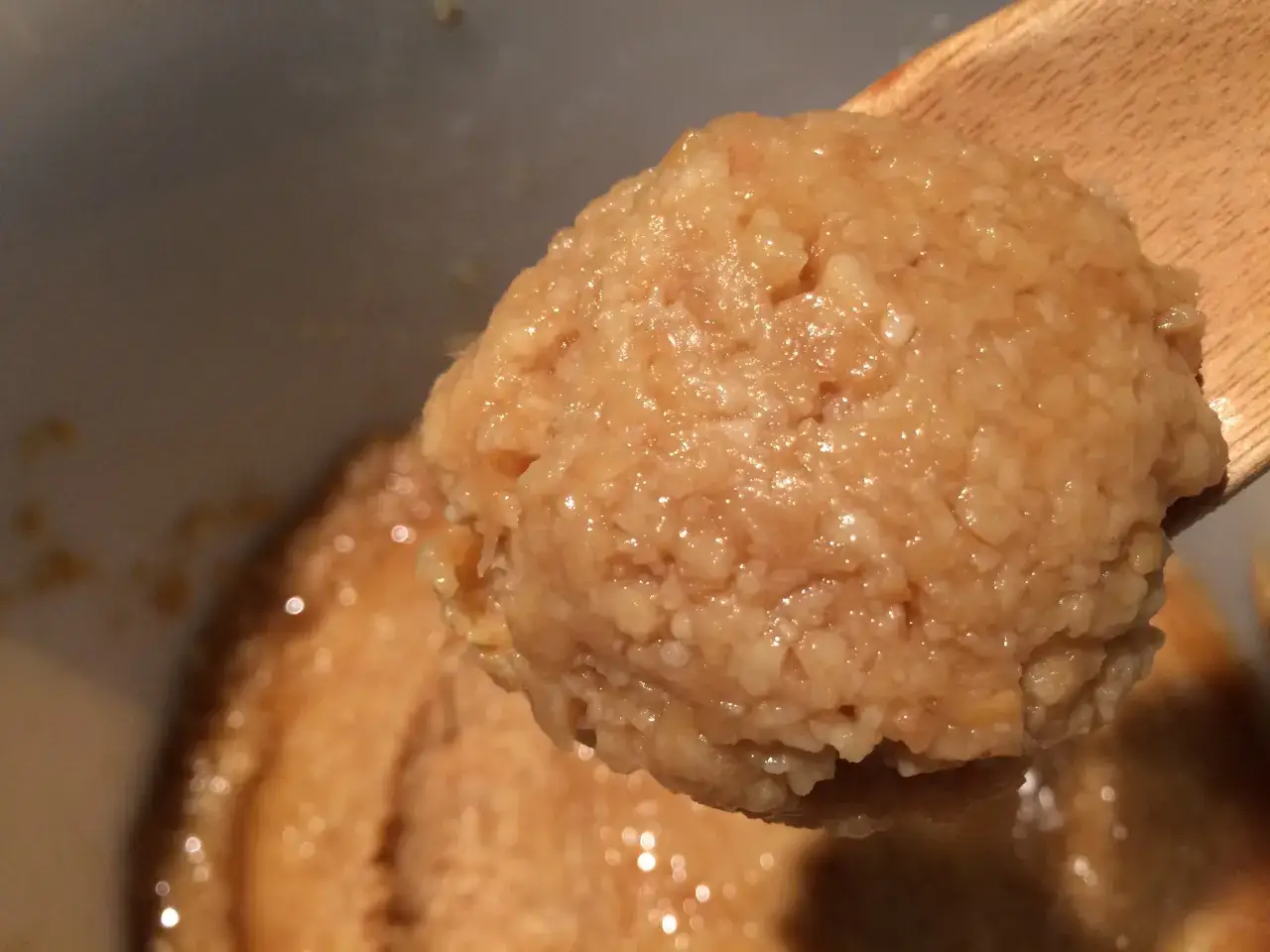 A wooden spoon scoops a portion of a textured, light brown mixture, likely part of a miso paste recipe.