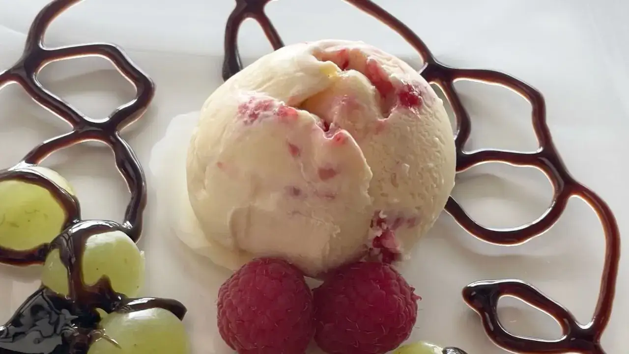 Ein cremiges Eis mit Zabaione Geschmack, verziert mit Himbeeren, Trauben und Schokoladensauce. Ein süßer Genuss!