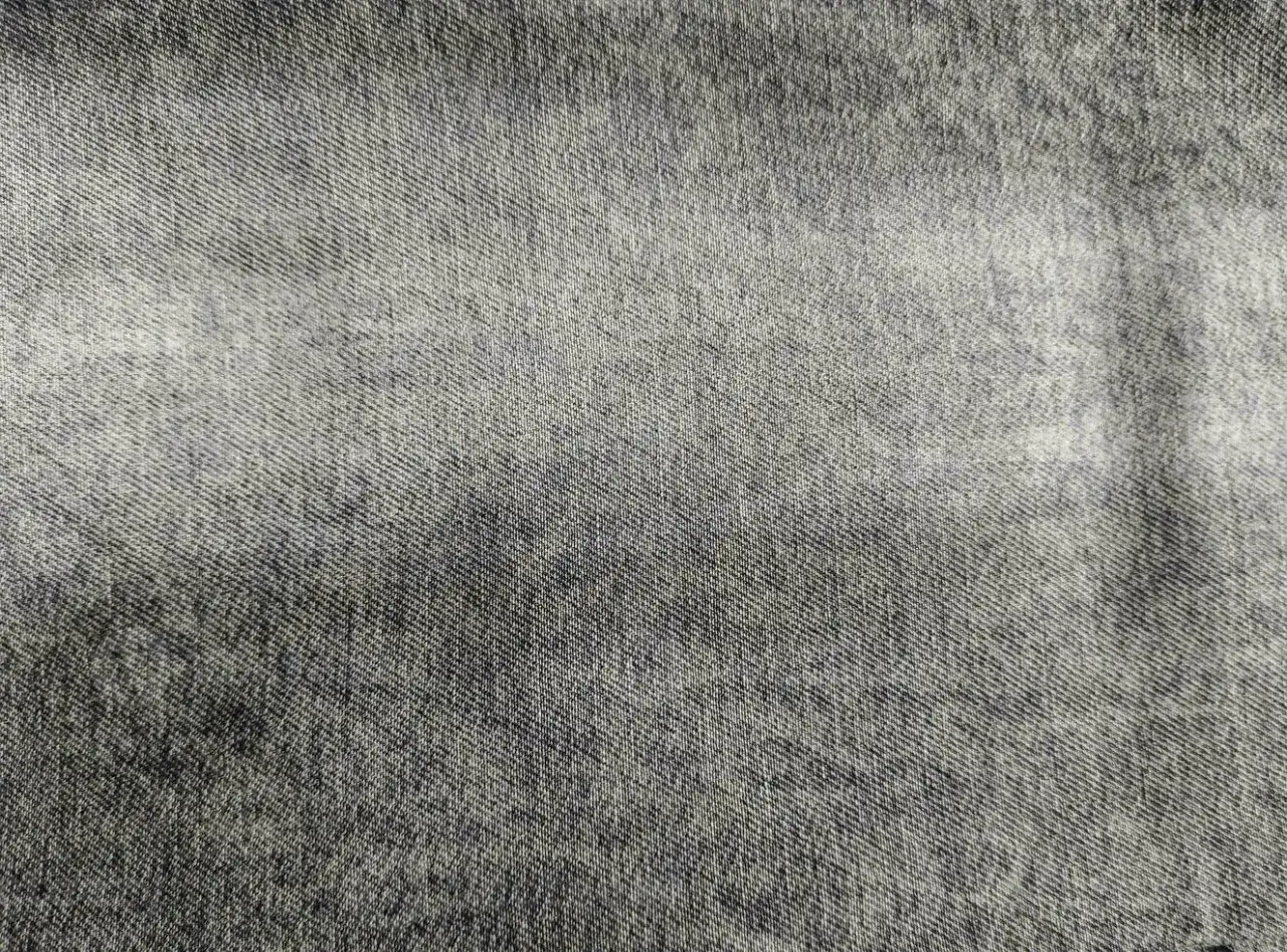 Texture di **denim** grigio chiaro con sfumature pi&ugrave; scure, che ricorda un tessuto vissuto e morbido.