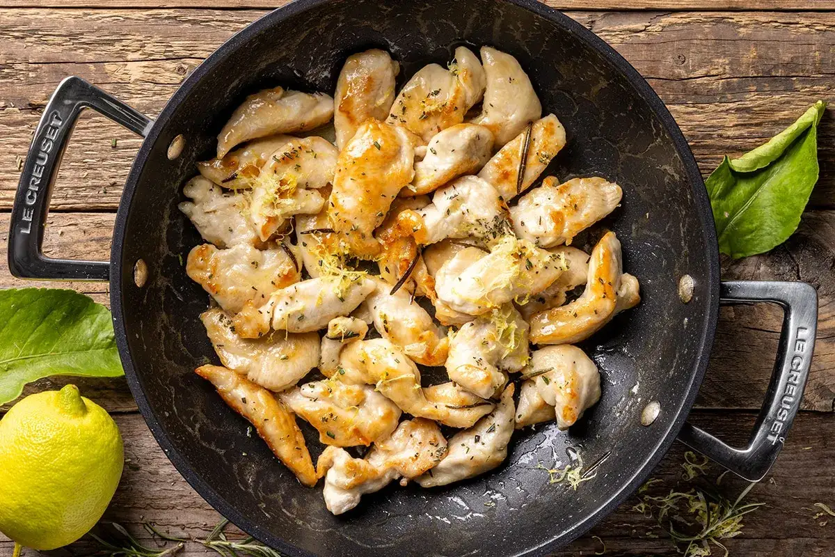 Straccetti di pollo dorati e succulenti, conditi con erbe aromatiche e scorza di limone, in una padella Le Creuset.