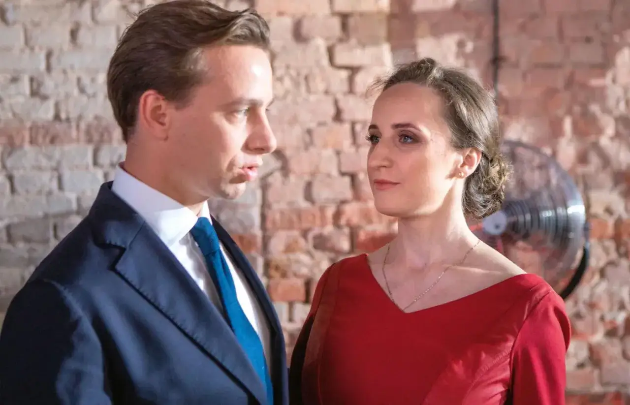 Krzysztof Bosak i jego żona w eleganckich strojach, w tle ceglana ściana i wentylator.