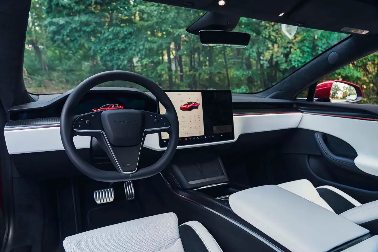 Wnętrze Tesla Model S z dużym ekranem dotykowym, minimalistyczną deską rozdzielczą i białymi skórzanymi fotelami.