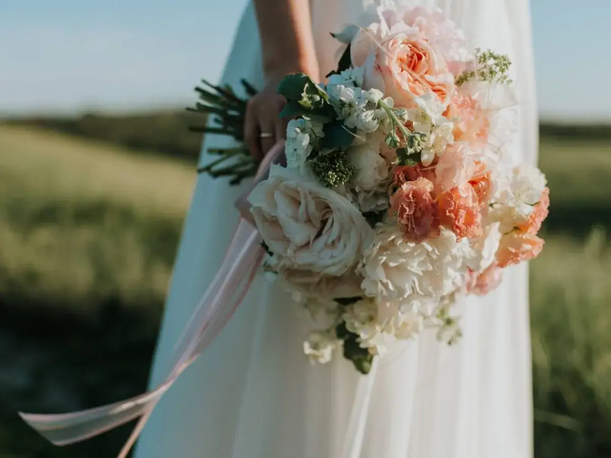 Un ramo de novia con rosas y peon&iacute;as en tonos pastel, la &uacute;ltima tendencia en ramos de novia, con cintas de seda cayendo.