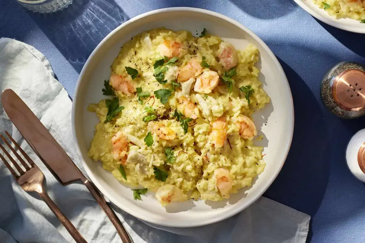 Kremowe risotto z krewetkami, ozdobione świeżą natką pietruszki i pieprzem. Idealne danie dla miłośników owoców morza.