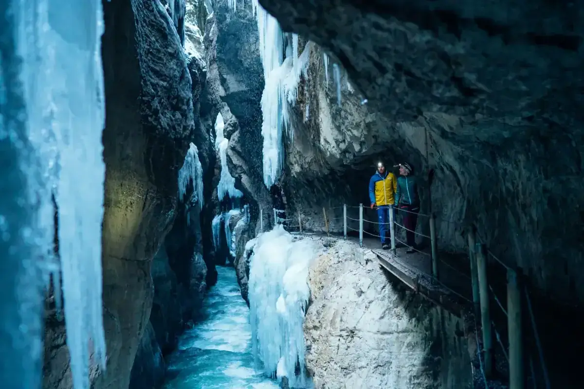 Zwei Wanderer erkunden die eisige Klamm Garmisch, umgeben von gefrorenen Wasserf&auml;llen und schroffen Felsw&auml;nden.