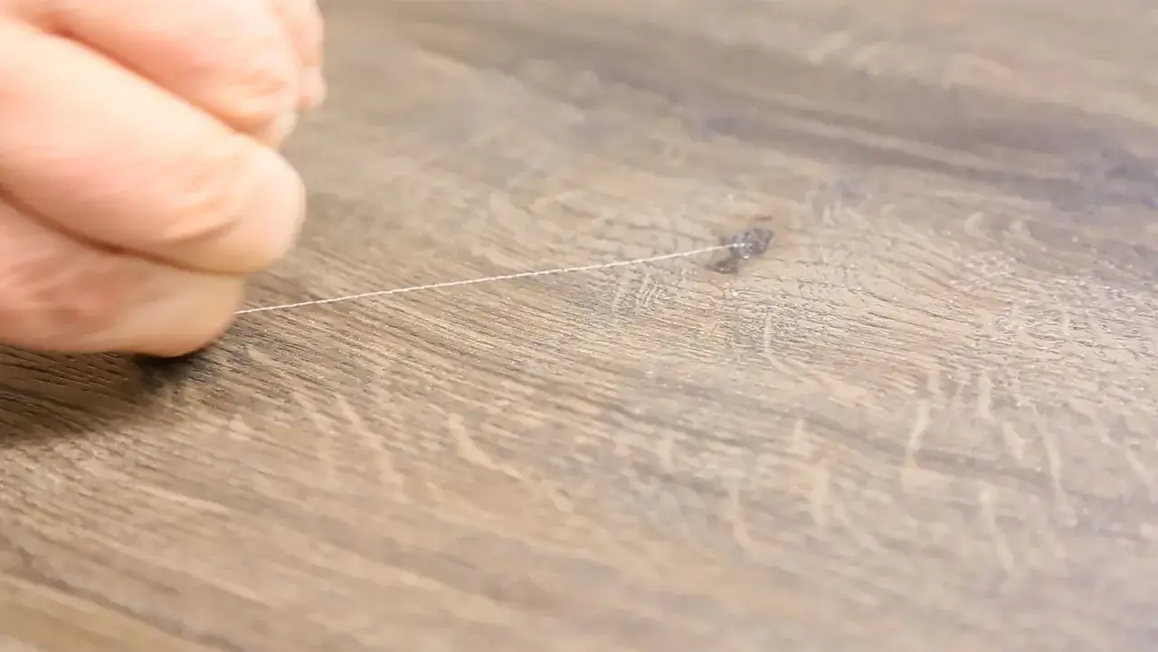 Un filo sottile evidenzia un graffio su un pavimento in PVC effetto legno, mostrando uno dei pavimenti in pvc svantaggi.