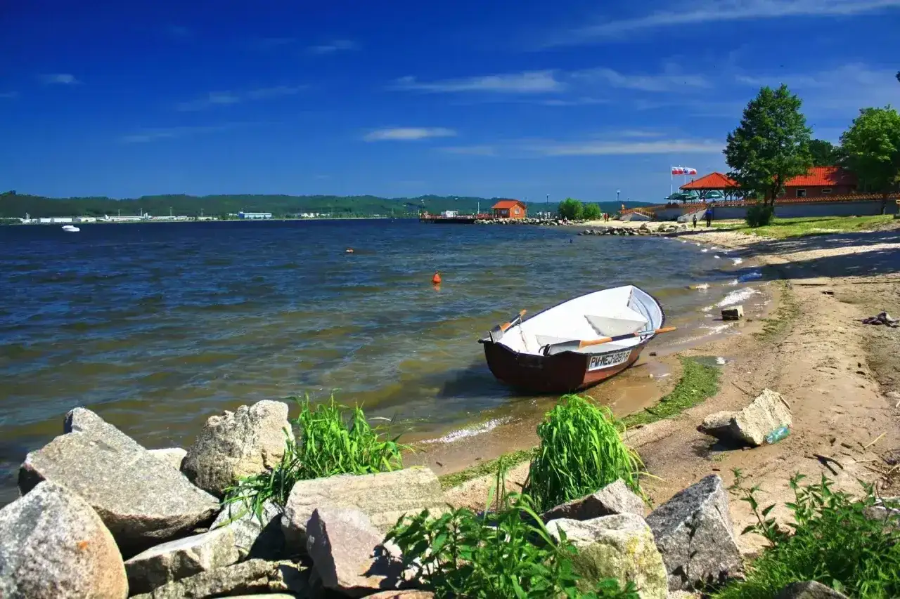 Ł&oacute;dka przy brzegu jeziora żarnowieckiego. Błękitne niebo, spokojna woda i piaszczysta plaża tworzą idylliczny krajobraz.