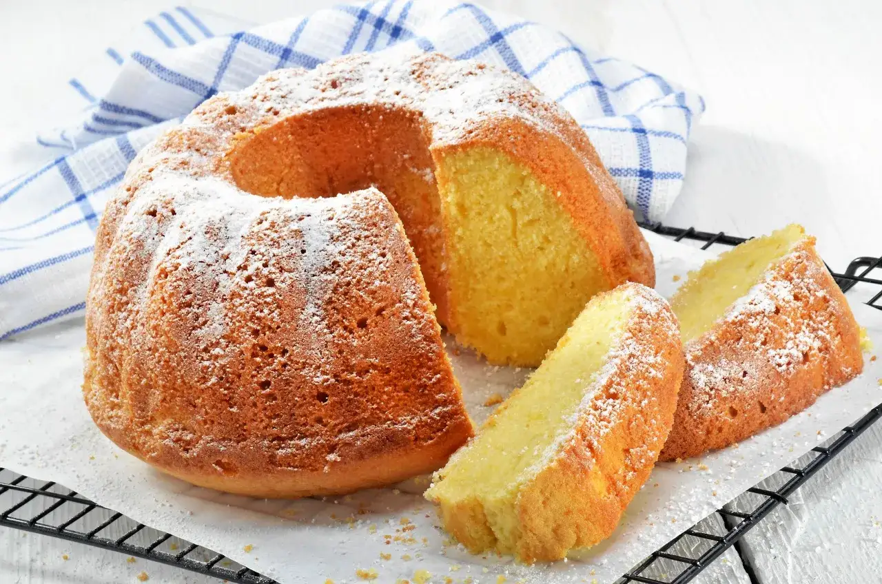 En gyllene sockerkaka, pudrad med florsocker, med två skivor upplagda. Perfekt för fika med mjuka kakor.