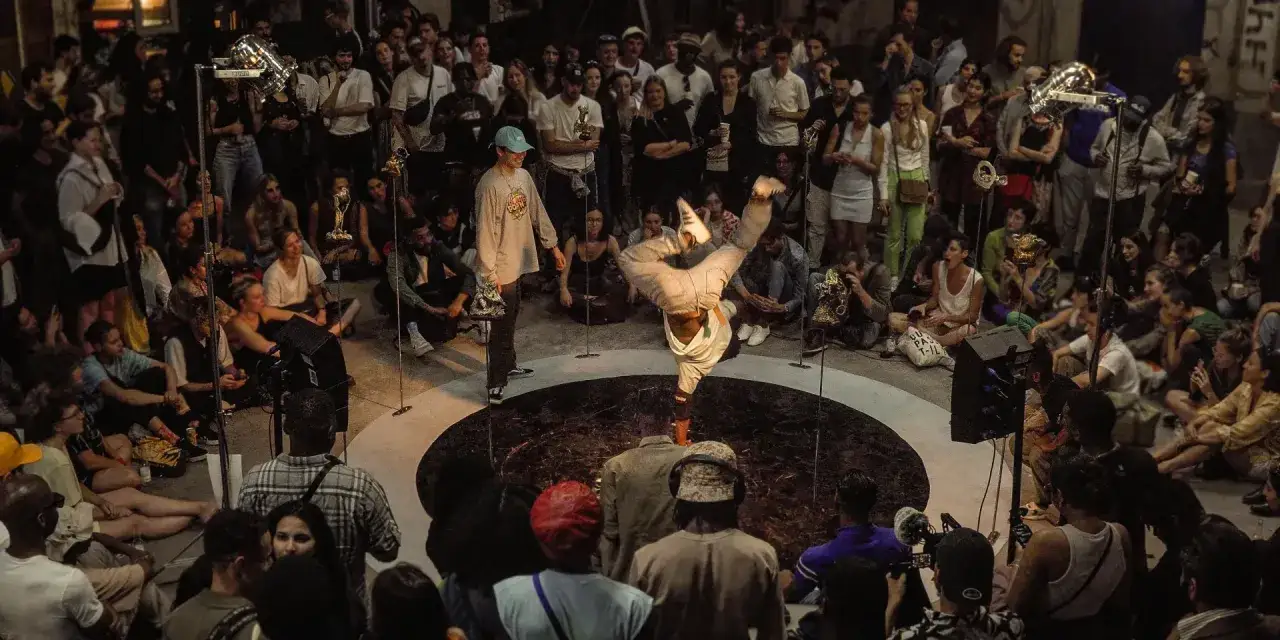 Un breakdancer en plein mouvement, un afro 93, captive une foule assise.