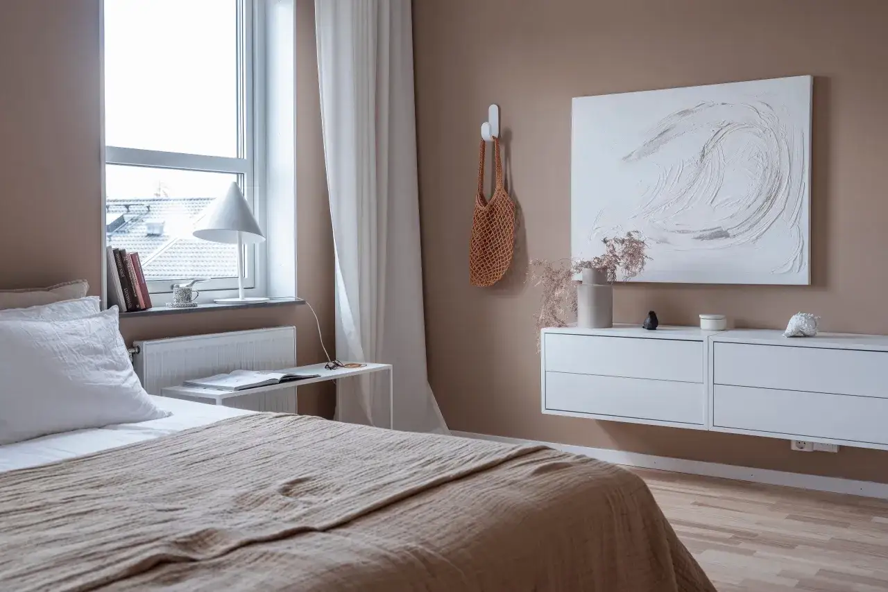 Mysig hotellrum inredning med säng, lampa, konst och en vägghängd byrå.