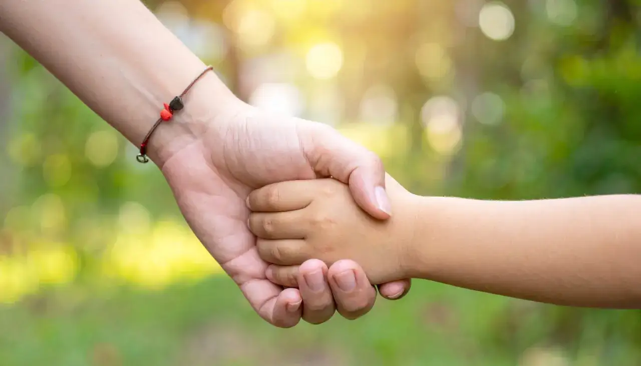 Eine Hand h&auml;lt die Hand eines Kindes. Das Band am Handgelenk der Erwachsenen erinnert daran, dass das Leben verg&auml;nglich ist, aber Liebe bleibt. Was bedeutet tot?