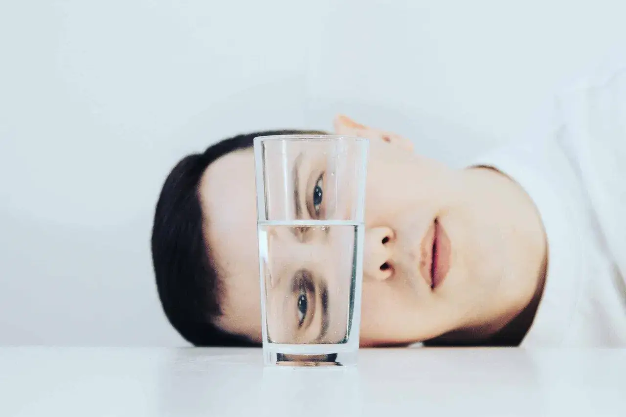 Un rostro se refleja en un vaso de agua, mostrando una dualidad entre lo pesimista y optimista.
