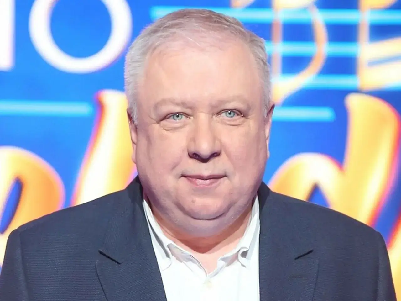 Marek Sierocki w garniturze, z niebieskimi oczami. W tle niebiesko-żółte litery.