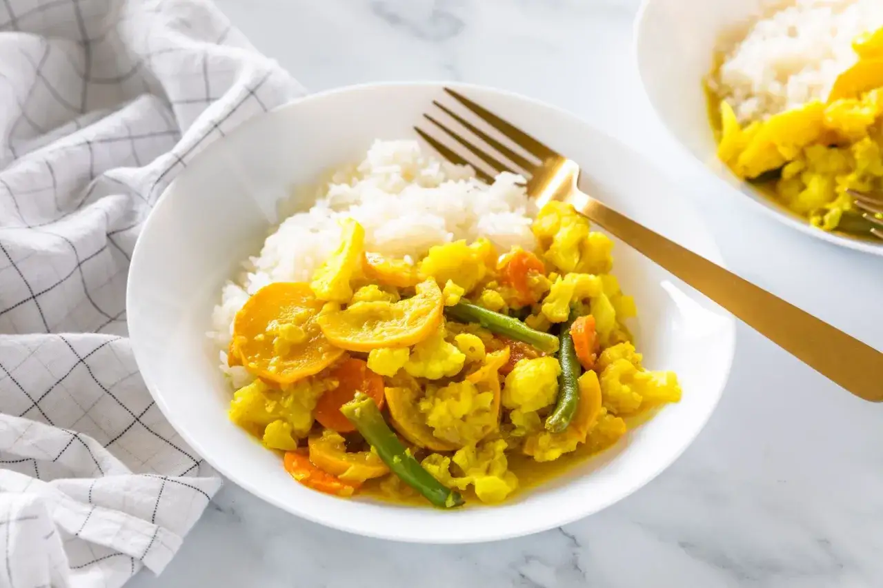 Un plat de riz blanc servi avec un curry de légumes coloré, composé de chou-fleur, carottes, courgettes et haricots verts.