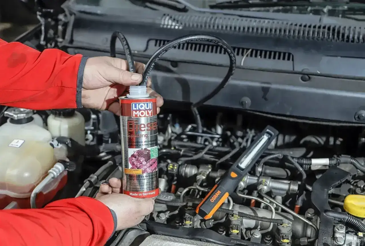 Mechanik używa preparatu do czyszczenia wtryskiwaczy diesel. Widać silnik i narzędzia.