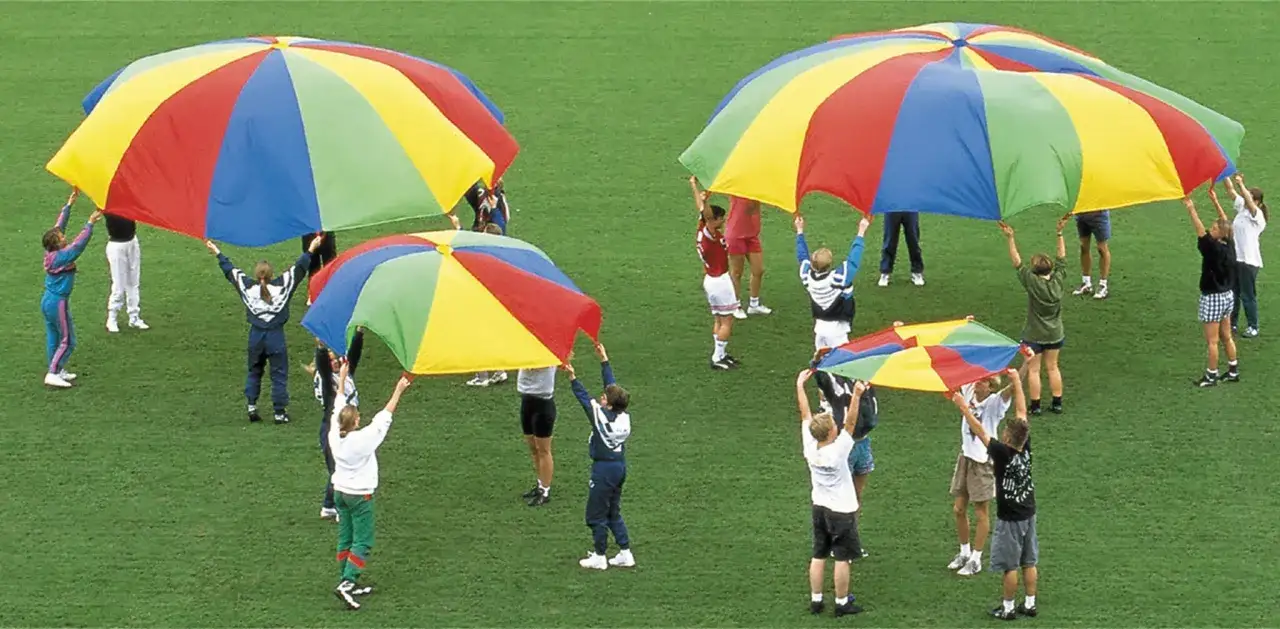 Kinder spielen bei den mini olympiade spielen mit bunten Fallschirmen auf einer grünen Wiese.